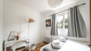 Quarto moderno com cama, escrivaninha com cadeira, radiador e janela com cortinas.