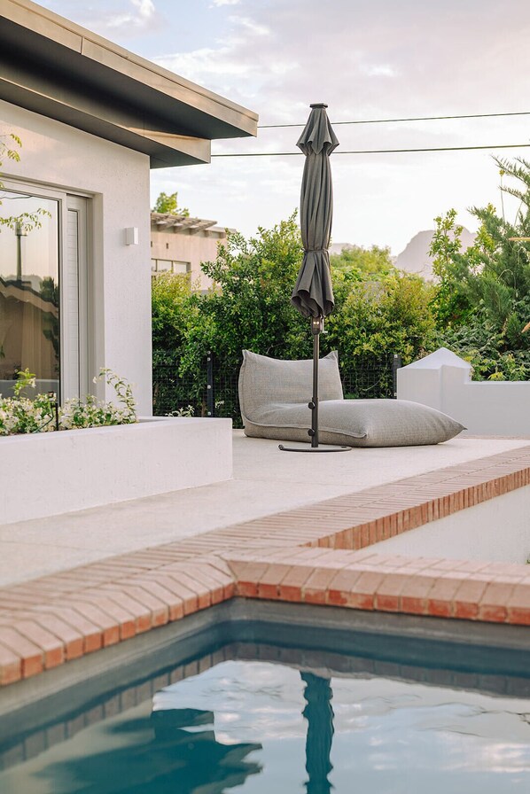 A swimming pool with a tiled edge, a lounge chair, and an umbrella. - Franschhoek Holiday Home for a family or friends traveling together (Franschhoek)