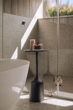 A modern bathroom with a large bathtub, a small round table with a candle and a glass container, and a glass shower enclosure. - Franschhoek Holiday Home for a family or friends traveling together (Franschhoek)
