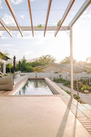 A covered outdoor area with a pool, a pergola, and a garden.