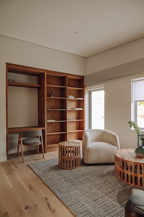 A modern living room with a wooden bookshelf, a grey armchair, a round wooden side table, and a patterned rug. - Franschhoek Holiday Home for a family or friends traveling together (Franschhoek)