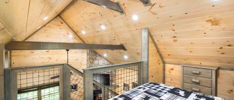 A wooden interior with a bed, a dresser, and a stone wall.