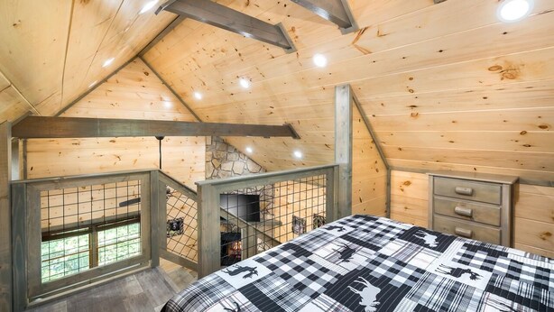 A wooden interior with a bed, a dresser, and a stone wall. - Lakeside Rendezvous (Gatlinburg)