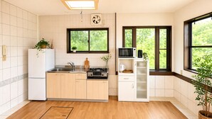 A modern kitchen with a central island, a built-in oven, and a microwave. There are windows providing natural light and views of greenery outside. - Peaceful Ocean View Villa with Free Parking & Full Kitchen (Miyazaki)