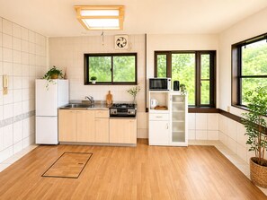 A modern kitchen with a central island, a built-in oven, and a microwave. There are windows providing natural light and views of greenery outside.