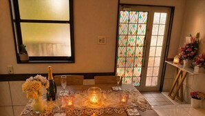 A dining table set with candles, a bottle, and flowers, with a window and a door in the background. - Peaceful Ocean View Villa with Free Parking & Full Kitchen (Miyazaki)