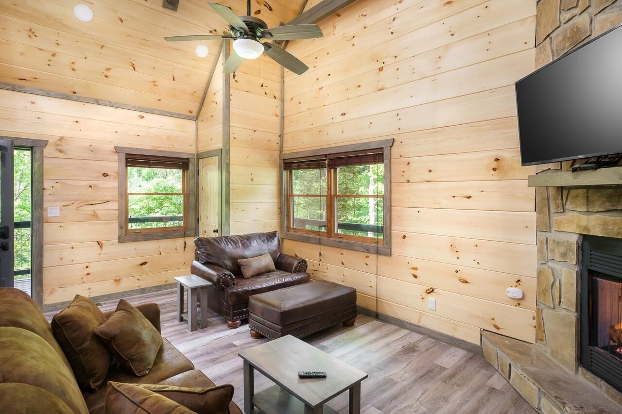 A wooden cabin interior with a leather sofa, ottoman, and a fireplace.