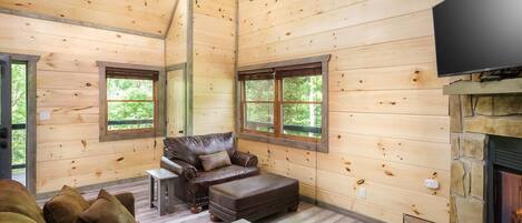 A wooden cabin interior with a leather sofa, ottoman, and a fireplace.