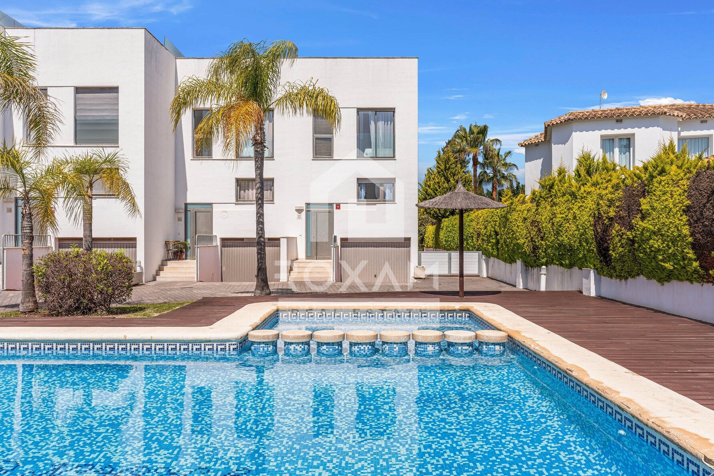 A modern building with a swimming pool, palm trees, and a tiled roof.. Townhouse in Oliva: Golf Views and Beach Nearby