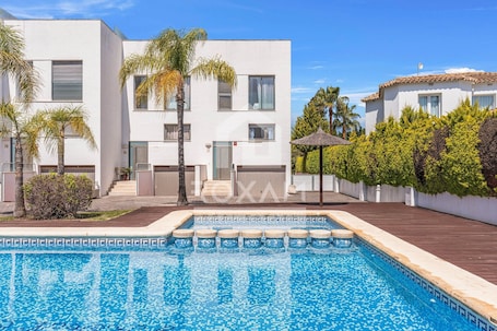 A modern building with a swimming pool, palm trees, and a tiled roof.. Townhouse in Oliva: Golf Views and Beach Nearby