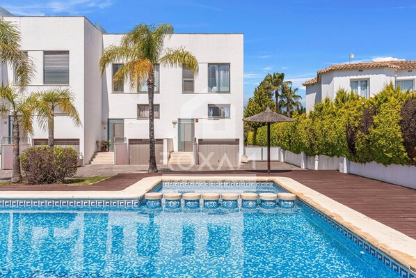 A modern building with a swimming pool, palm trees, and a tiled roof. - Townhouse in Oliva: Golf Views and Beach Nearby (Molinell)