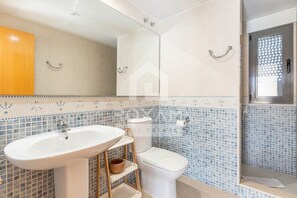 A bathroom with a sink, toilet, and shower area, featuring tiled walls and a wooden door. - Townhouse in Oliva: Golf Views and Beach Nearby (Molinell)