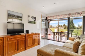 Ein modernes Wohnzimmer mit Flachbildfernseher, Holzkredenz, einer Couch und einem Balkon mit Gartenmöbeln.