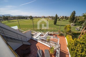 A residential property with a terrace, a view of a green field, and distant mountains.