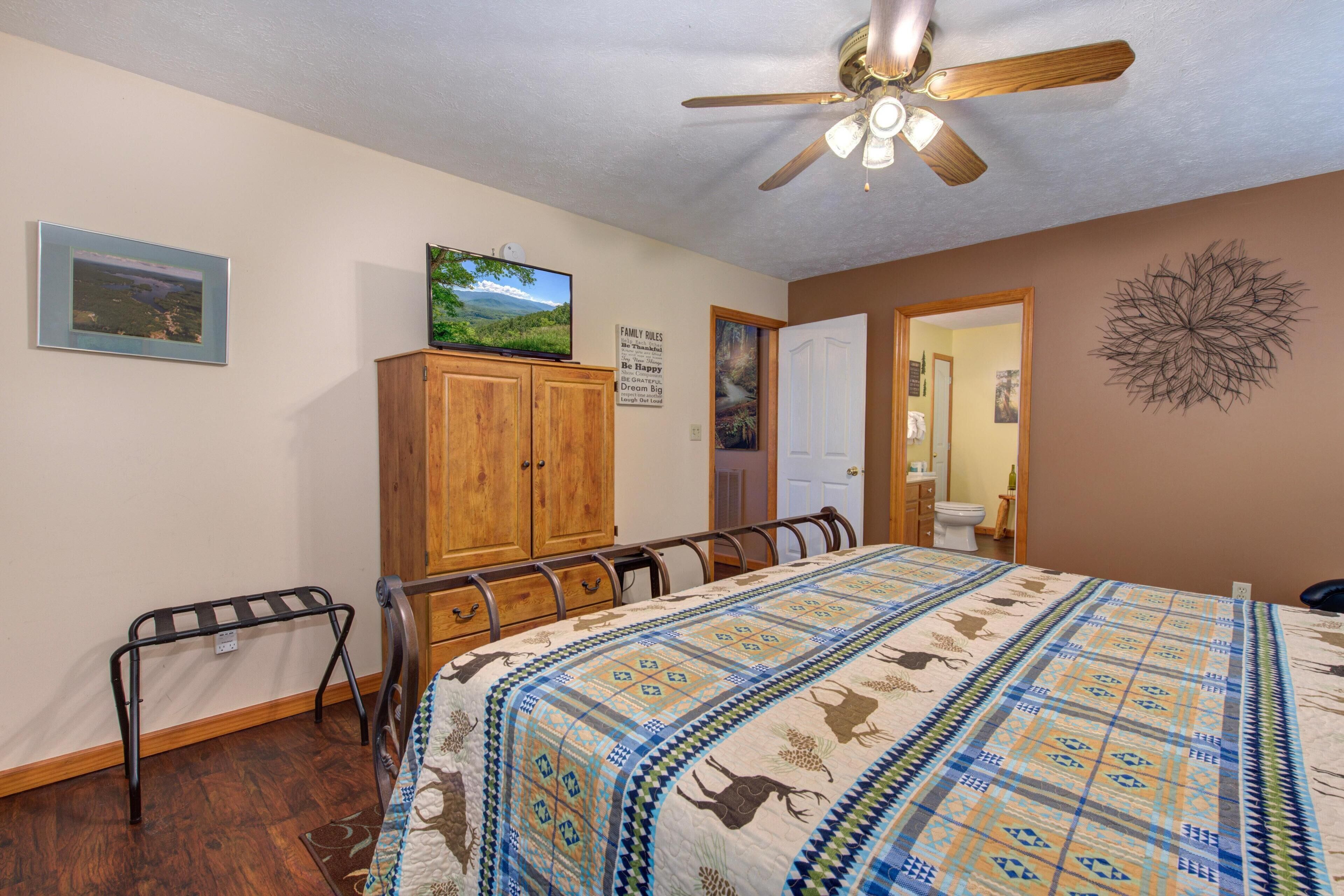 A bedroom with a bed, wooden wardrobe, ceiling fan, and a television on a cabinet.