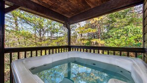 Een hottub met een houten terras en uitzicht op een bos.