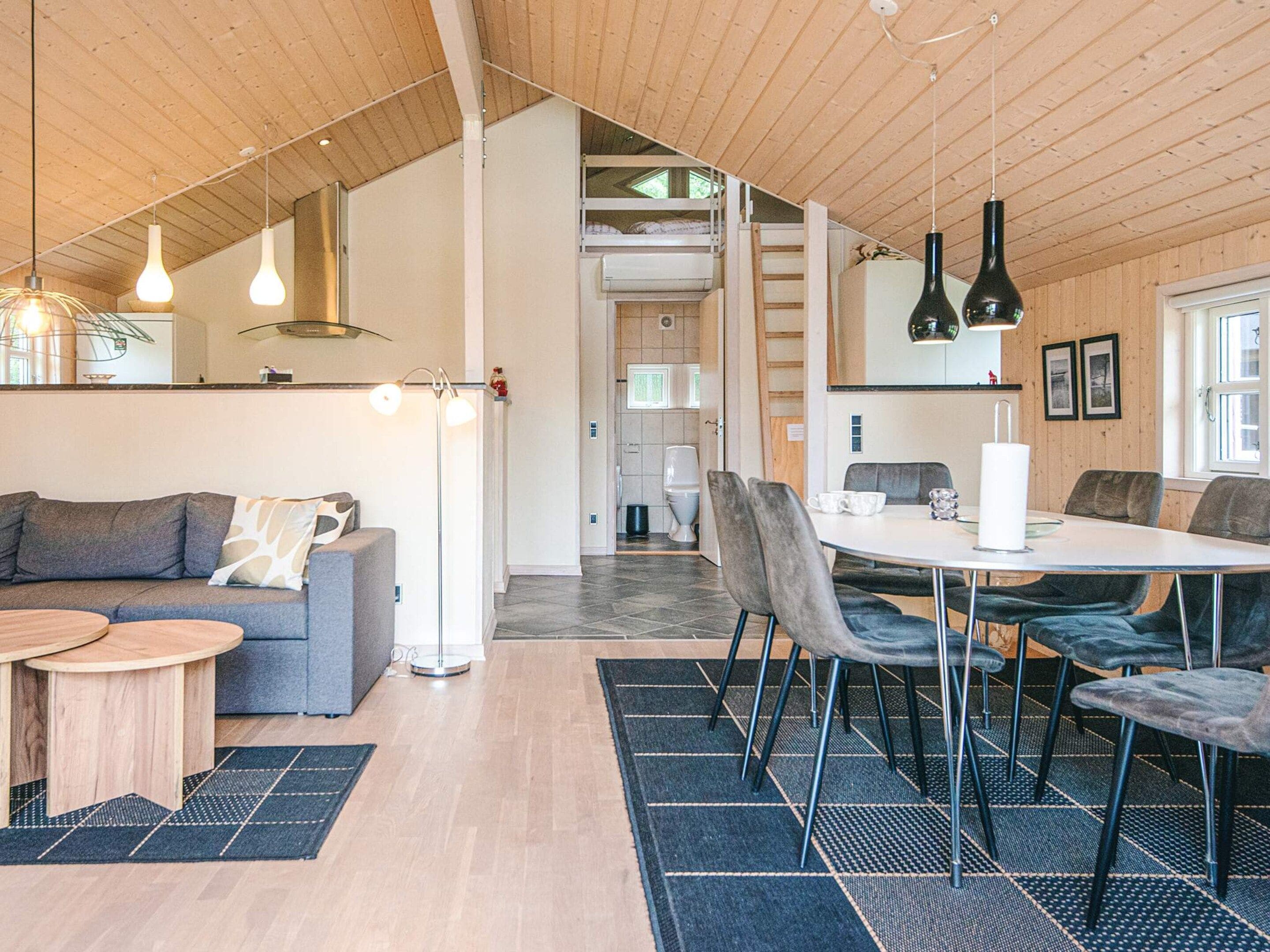 Un interno moderno con zona pranzo, cucina e camera soppalco con soffitto in legno.