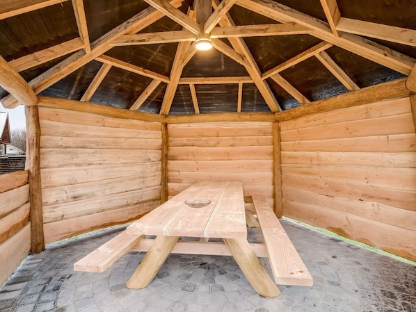 Una cabaña de madera con techo a dos aguas, una mesa de madera en el centro y suelo de baldosas de piedra.