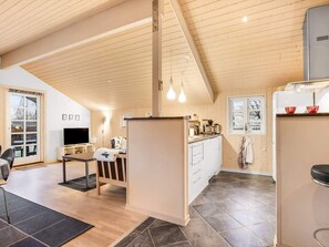Un intérieur moderne avec un plafond en bois, un coin cuisine, un espace repas et un téléviseur.