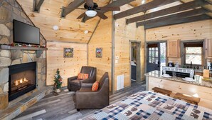A log cabin interior with a fireplace, a television, a cozy seating area, and a kitchen. - Serenity Studio (Gatlinburg)