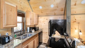 A kitchen with wooden cabinets, granite countertops, a black refrigerator, and a stove. - Serenity Studio (Gatlinburg)