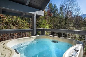 A hot tub with a wooden deck, surrounded by trees and a clear sky. - Serenity Studio (Gatlinburg)