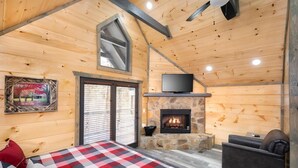 A cozy cabin interior with a stone fireplace, a television, and a checkered bedspread. - Solitude Studio (Gatlinburg)