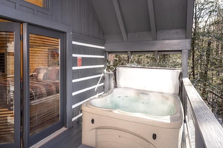 A hot tub on a wooden deck with a glass door and window, surrounded by trees.. Solitude Studio