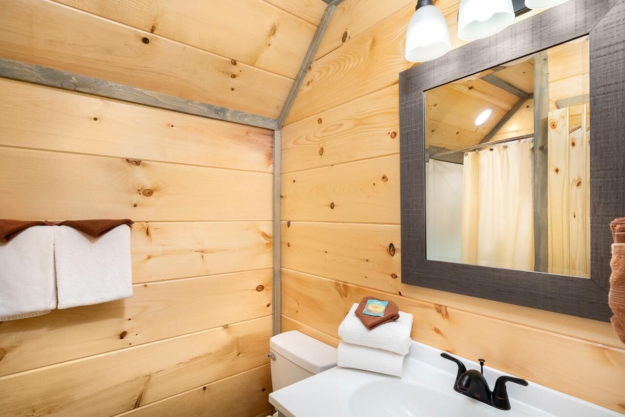 Un baño rústico con cabaña, con un lavamanos blanco, un espejo y un perchero para toallas.