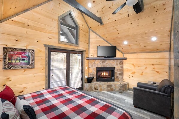 Ein gemütliches Blockhaus-Interieur mit Kamin aus Stein, einem Fernseher und einer karierten Bettdecke.