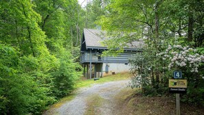 Een grindpad leidt naar een gebouw, omringd door weelderige groene beplanting. Een bord geeft de locatie aan als 'Stony Brook Sunset Studio'.