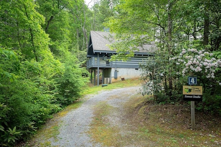 A gravel path leading to a building surrounded by dense green foliage. A sign indicates the location as 'Stony Brook Sunset Studio.'. Sunset Studio