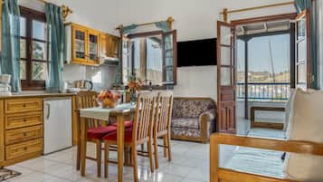 A kitchen with wooden cabinets, a dining table with chairs, a sofa, and a bed.