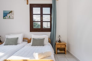 Ein Schlafzimmer mit zwei Betten, einem hölzernen Kopfteil, einem Nachttisch mit Lampe, einem Fenster mit Vorhängen und einem Bild an der Wand.
