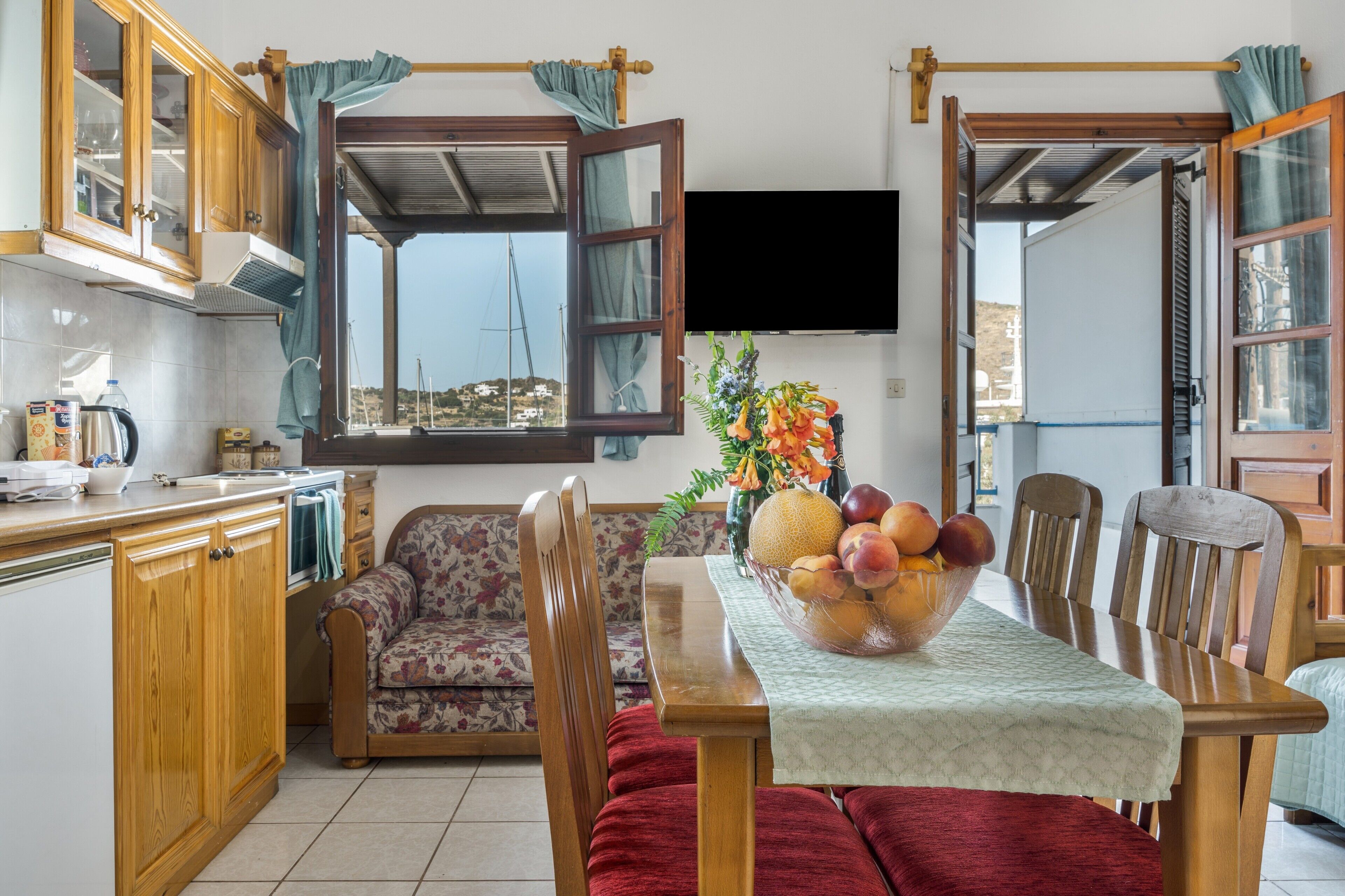 A kitchen with a dining area, wooden cabinets, a sofa, and a table with a fruit bowl.