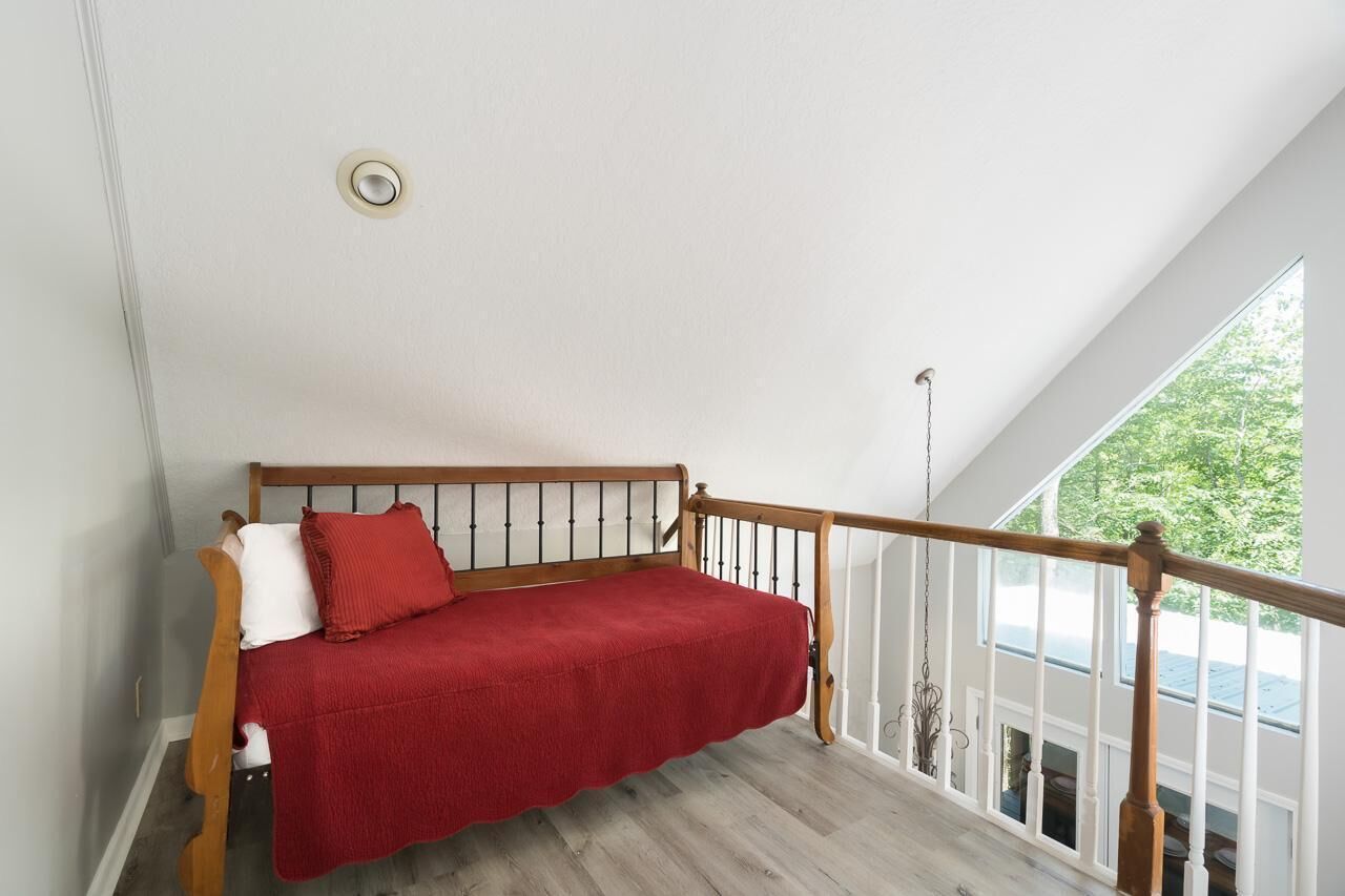 A loft bedroom with a wooden bed, white walls, and a view of greenery outside.