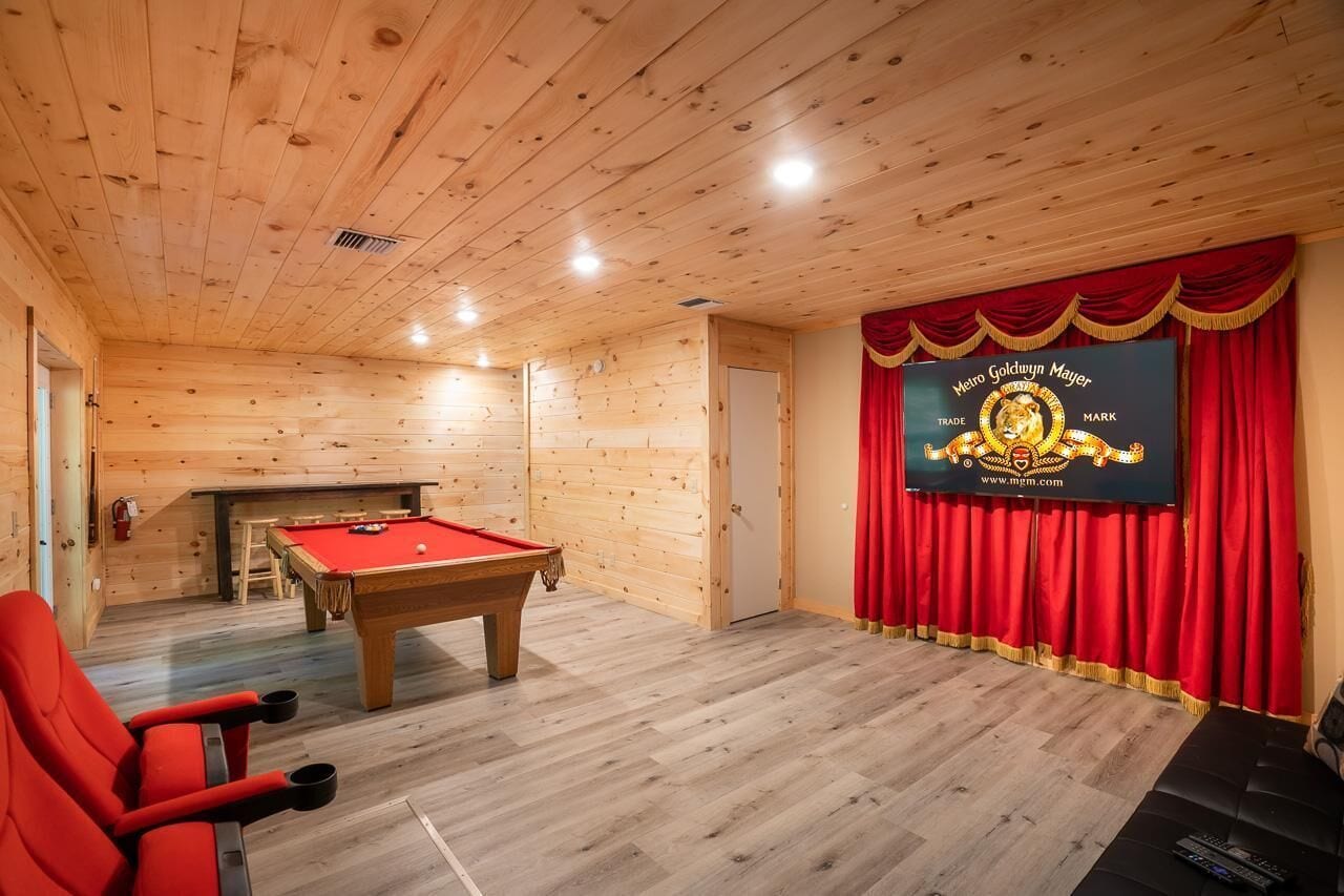 Una habitación de madera con mesa de billar, cortinas rojas y un cartel en la pared.