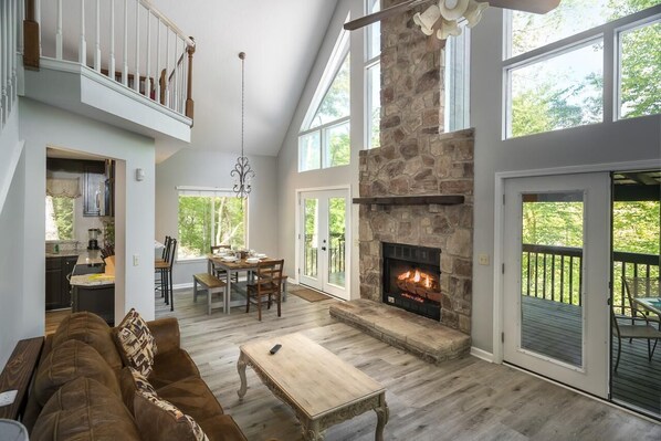 A spacious living room with a stone fireplace, a dining area, and a staircase leading to an upper level. - Autumn Breeze (Gatlinburg)