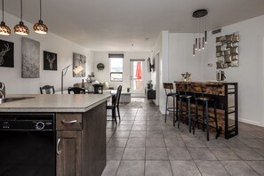 A modern kitchen with a central island, bar stools, pendant lighting, and a dining area with a sofa and chairs. - Breathe taking resort in the heart of the Lower Mission. (Kelowna)