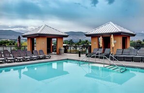 A pool area with lounge chairs and two small structures, likely restrooms, with a view of mountains in the background. - Breathe taking resort in the heart of the Lower Mission. (Kelowna)