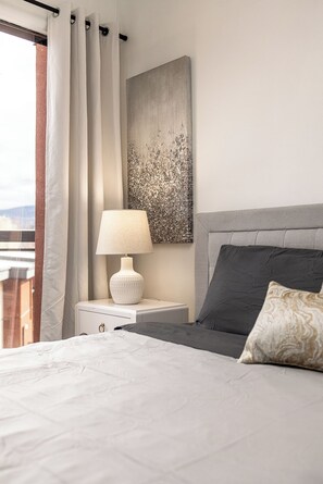 A bedroom with a bed, a nightstand with a lamp, a headboard, and a painting on the wall. - Breathe taking resort in the heart of the Lower Mission. (Kelowna)