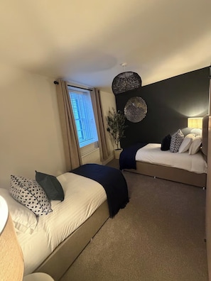 Un dormitorio con dos camas, una ventana con cortinas, una lámpara de pared y una planta en maceta.