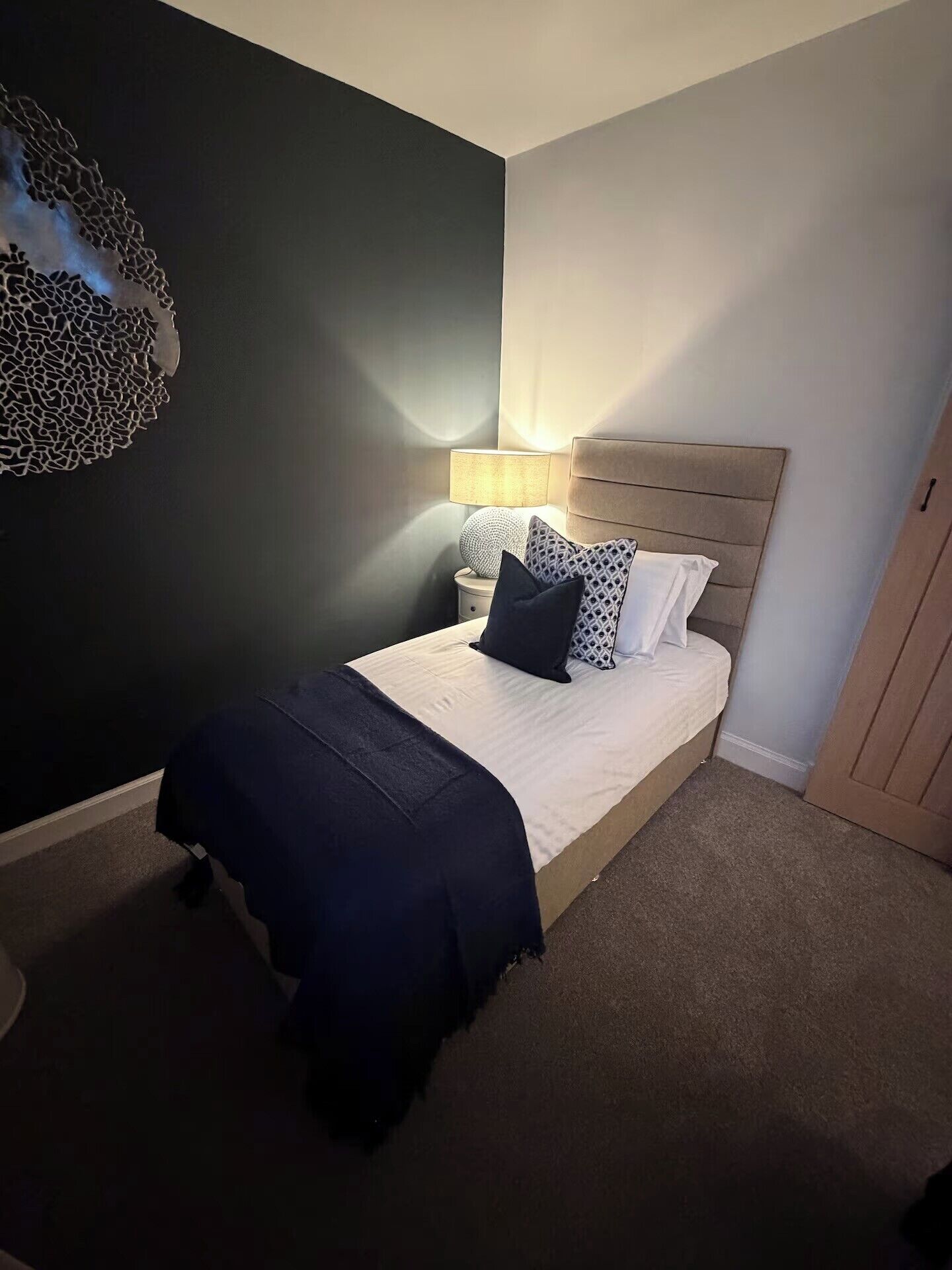 Een slaapkamer met een bed, een bedlampje en een kunstwerk aan de muur.
