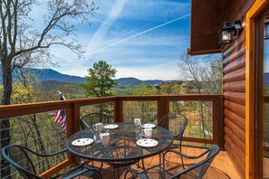 Une terrasse en bois avec une table et des chaises, offrant une vue sur un paysage montagneux.