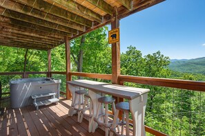 Une terrasse en bois avec un jacuzzi, des tabourets de bar et un panneau d’avertissement indiquant la présence d’ours dans la zone.