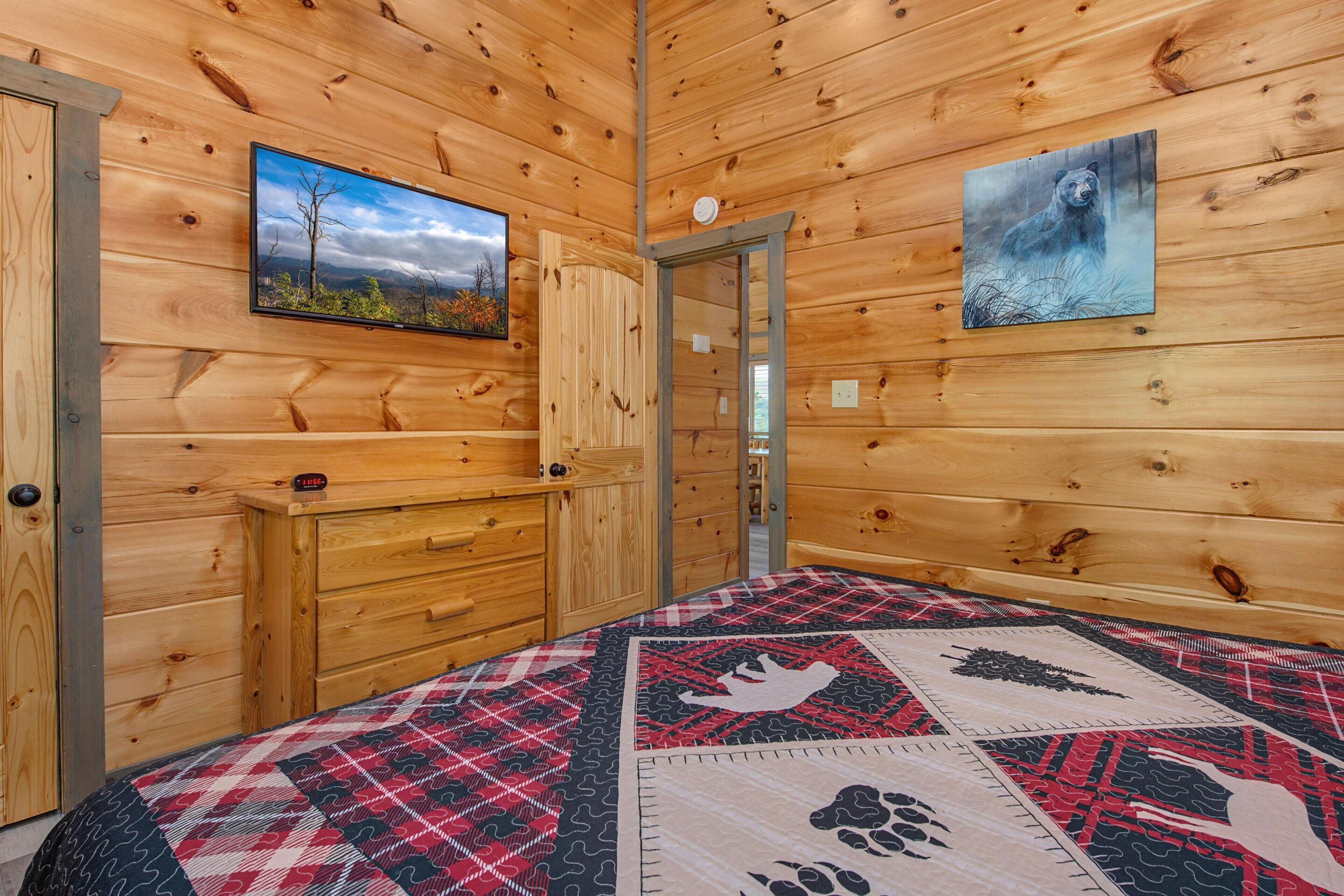 Ein Zimmer in einer Holzhütte mit einem Bett, einer Kommode, einem Fernseher und einem Bärenbild.