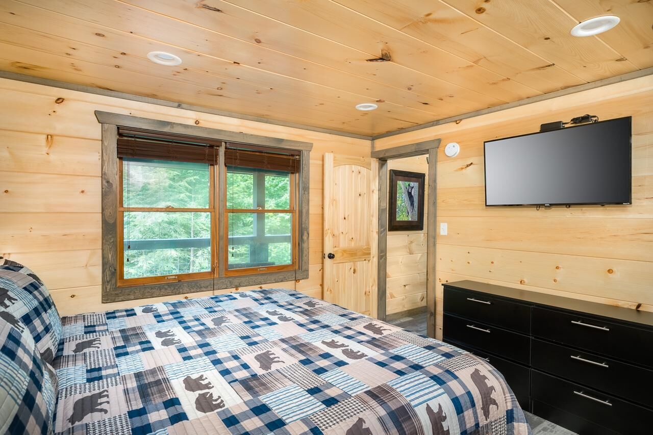 Ein Schlafzimmer einer Holzhütte mit einem Bett, einem Fernseher und einem Fenster.