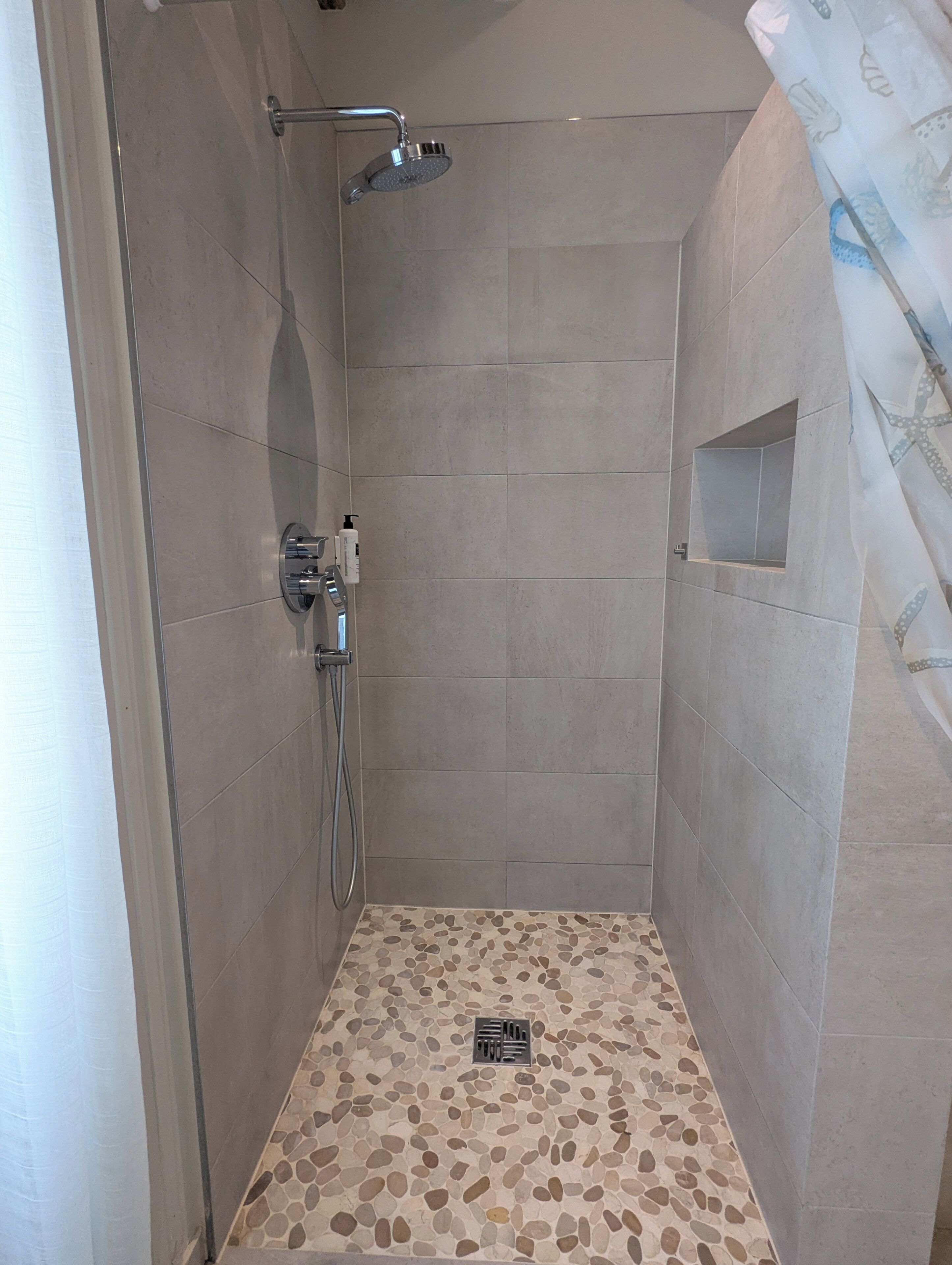 A shower with a handheld showerhead, a wall-mounted faucet, and a small shelf.