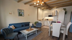 A modern living room with a blue sofa, a coffee table, and a dining area with a white table and chairs. - Ideal for families, couples and relaxing holidays, swimming pool, quiet, authentic. (Julienne)