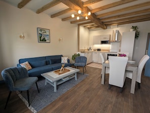 A modern living room with a blue sofa, a coffee table, and a dining area with a white table and chairs. - Ideal for families, couples and relaxing holidays, swimming pool, quiet, authentic. (Julienne)